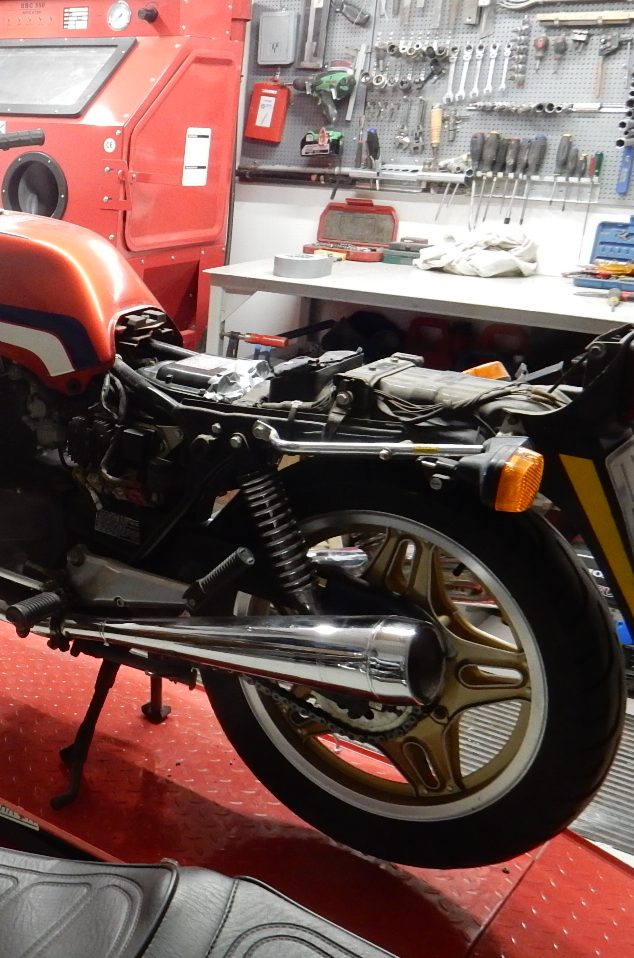 Står på en elhydralisk mc lyft Motorcykel i verkstad med röd och vit färg, delvis demonterad.